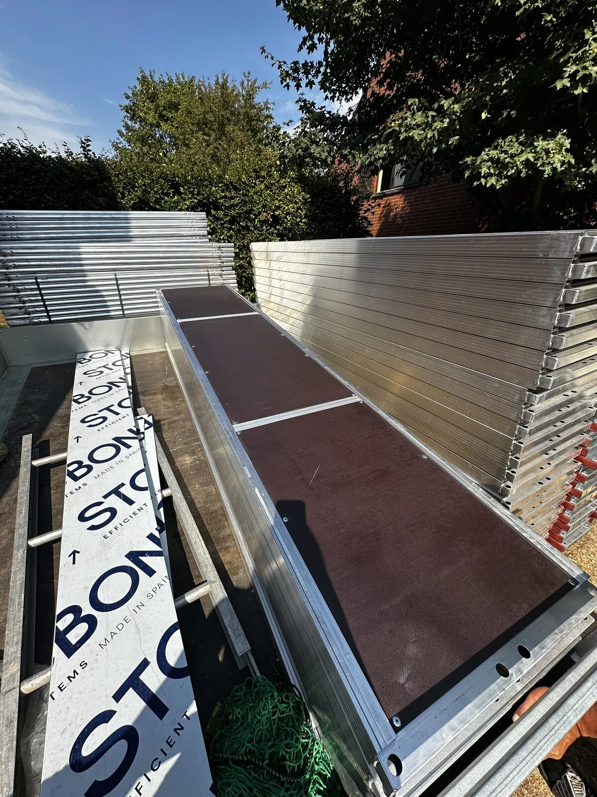 Pile de planchers d'échafaudage en aluminium stockée en extérieur le long d'une clôture